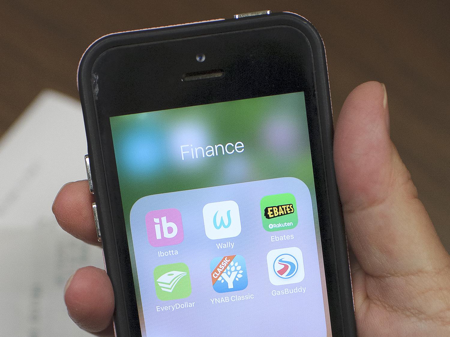 A hand holds a smartphone displaying finance apps on its screen.