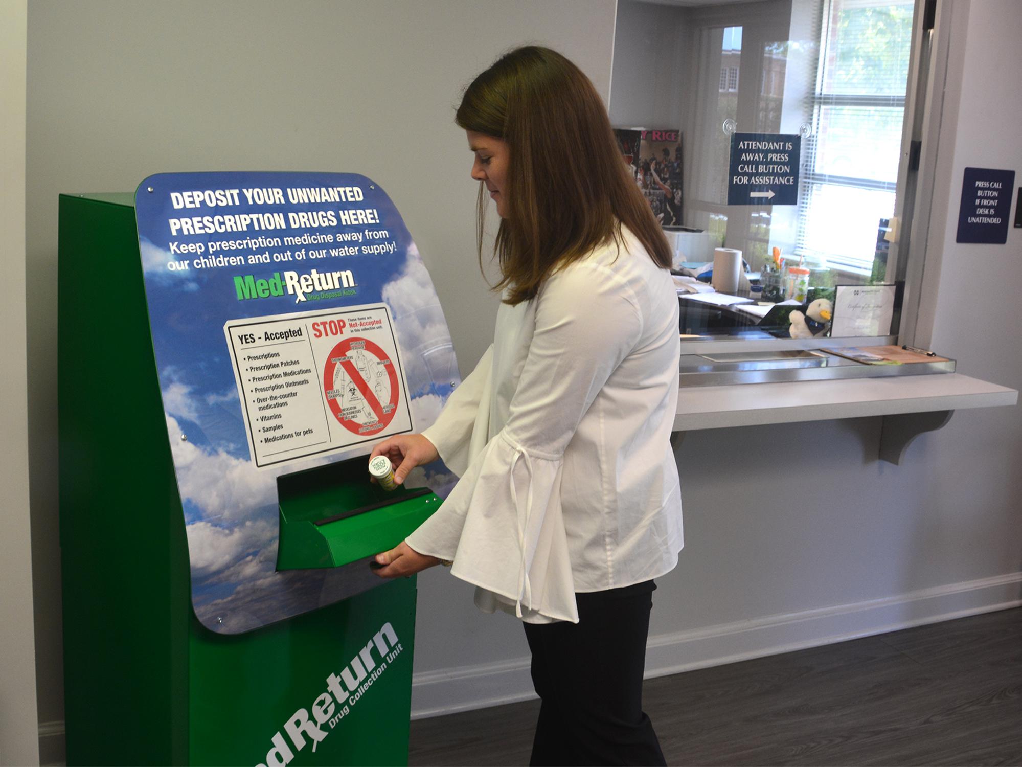 Young woman places a prescription bottle in secure slot in a large, green metal box