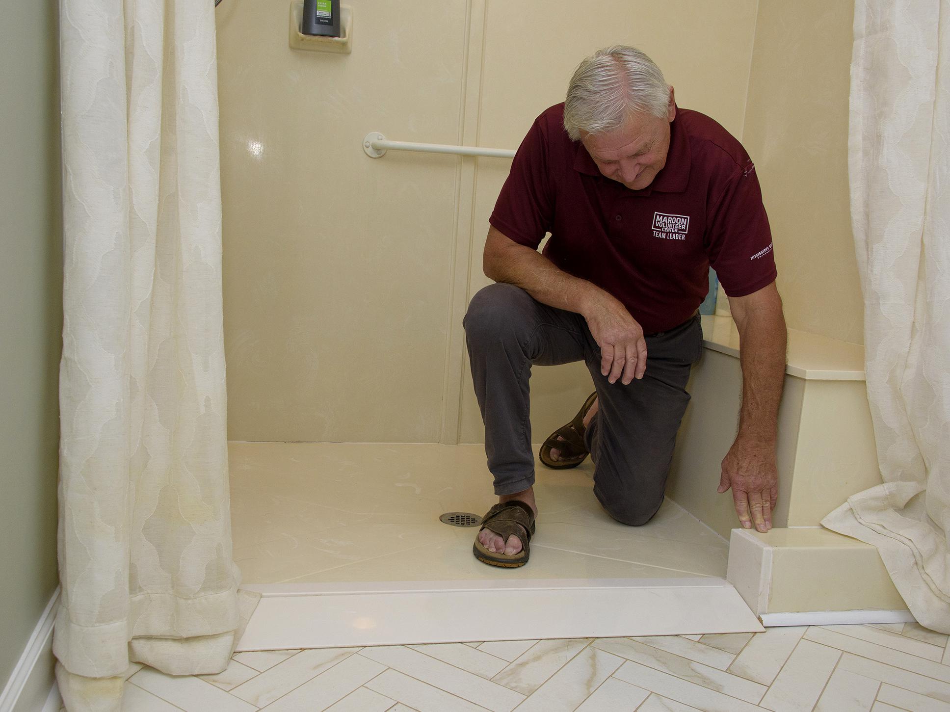 A man kneels in a walk-in shower, reaching down to a point in the entryway.