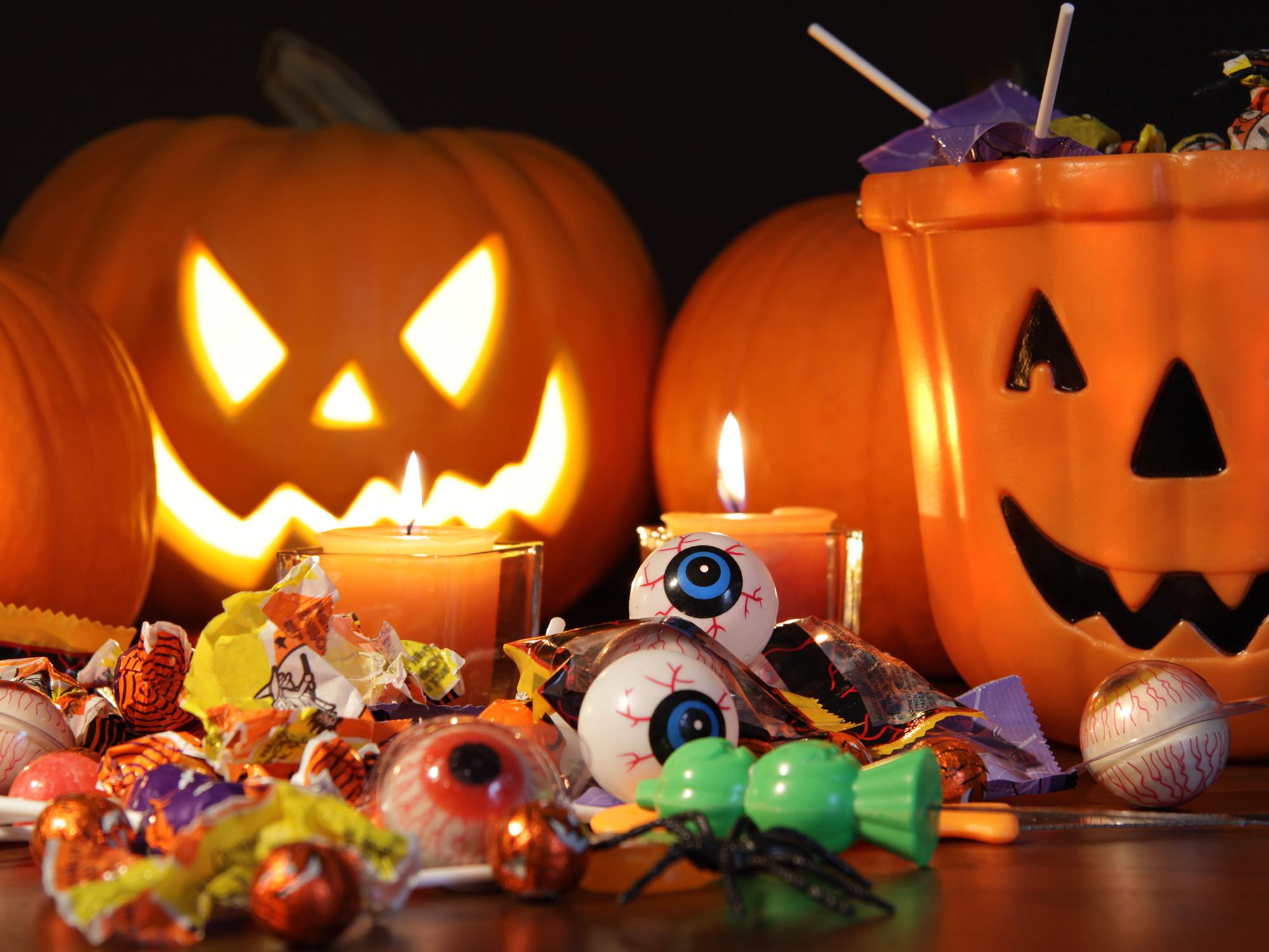 Orange pumpkins and a carved jack-o-lantern sit on a table behind a smiling ceramic jack-o-lantern candy dish. Toys, candy and candles are displayed in front of the pumpkins.