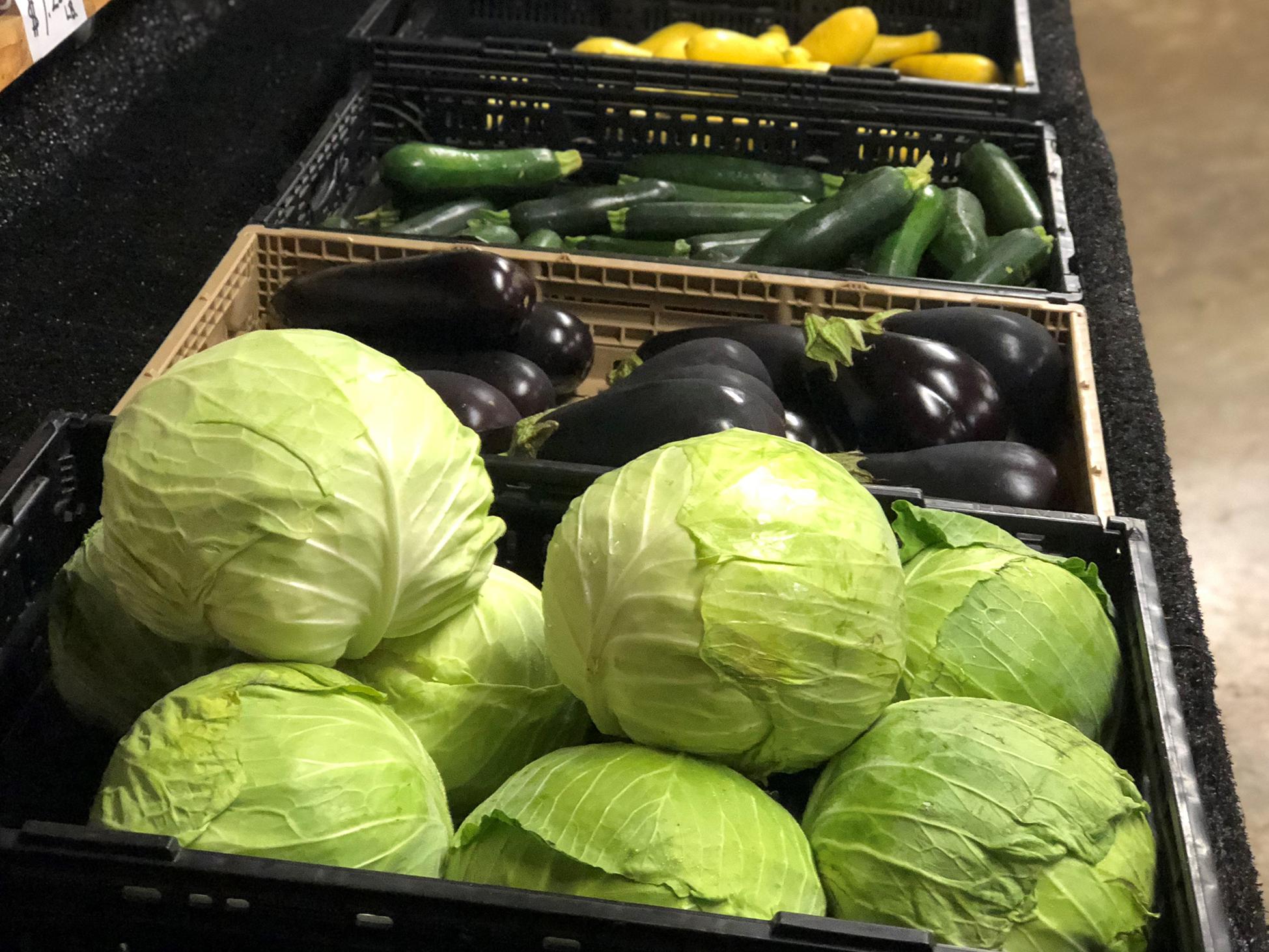 Light green lettuce, dark purple eggplant and cucumbers sit on black shelves.