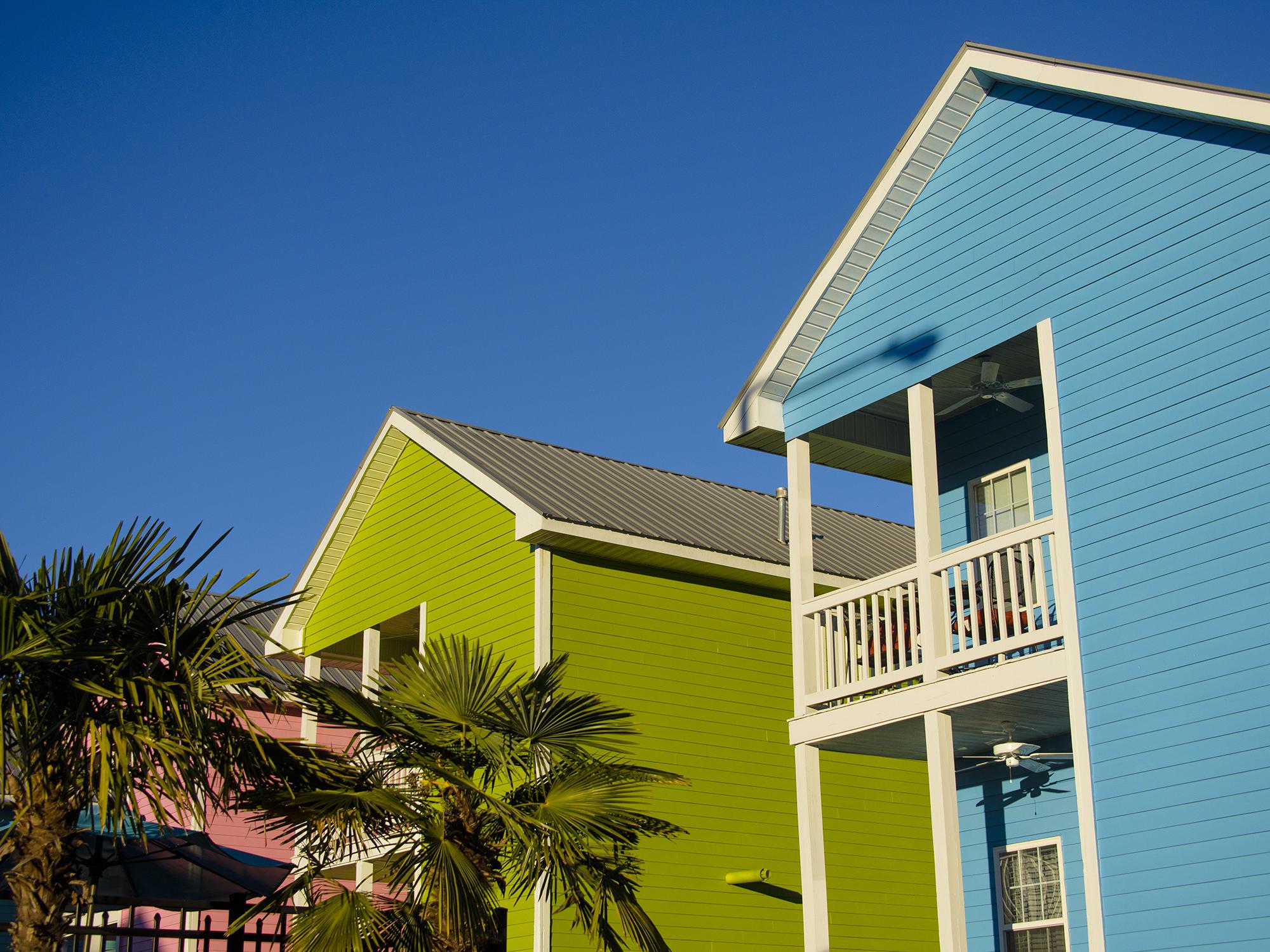 Palm trees adorn the landscape in front of blue, green and pink cottages.
