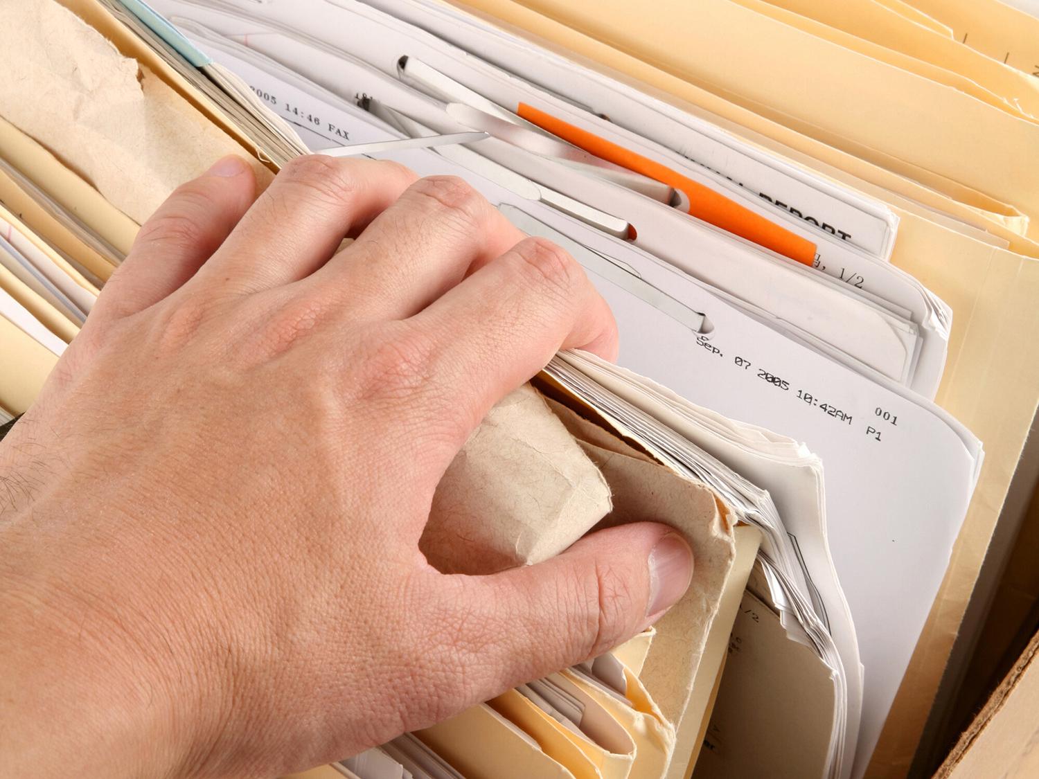 A man’s hand reaches into a box of files, pulling back the corner of one folder.