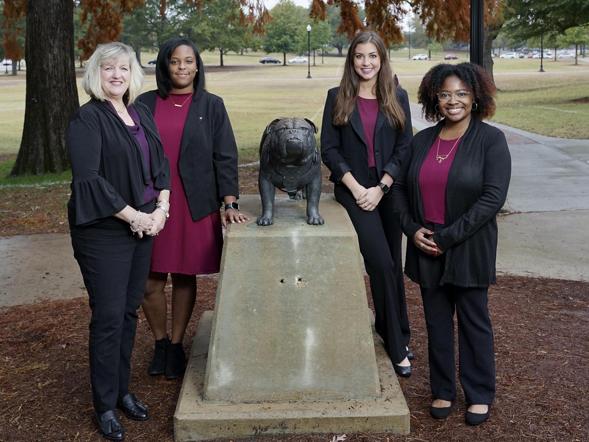 Four women stand around the Bully statue on the Mississippi State University campus.