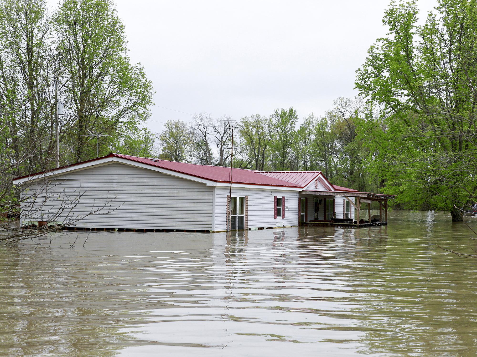 A gray, double-wide manufactured home with flood waters reaching the lower windows and surrounding area