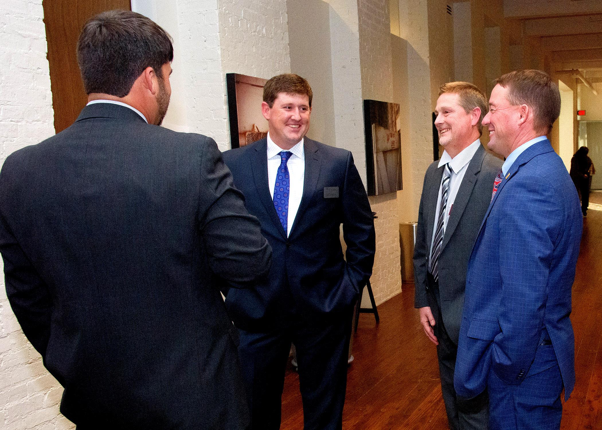 Four men in business suits talking to each other and laughing.