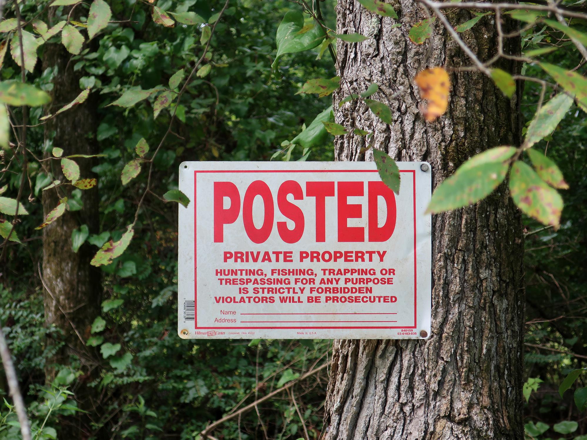 A private property sign is nailed to a tree with vegetation in the background.