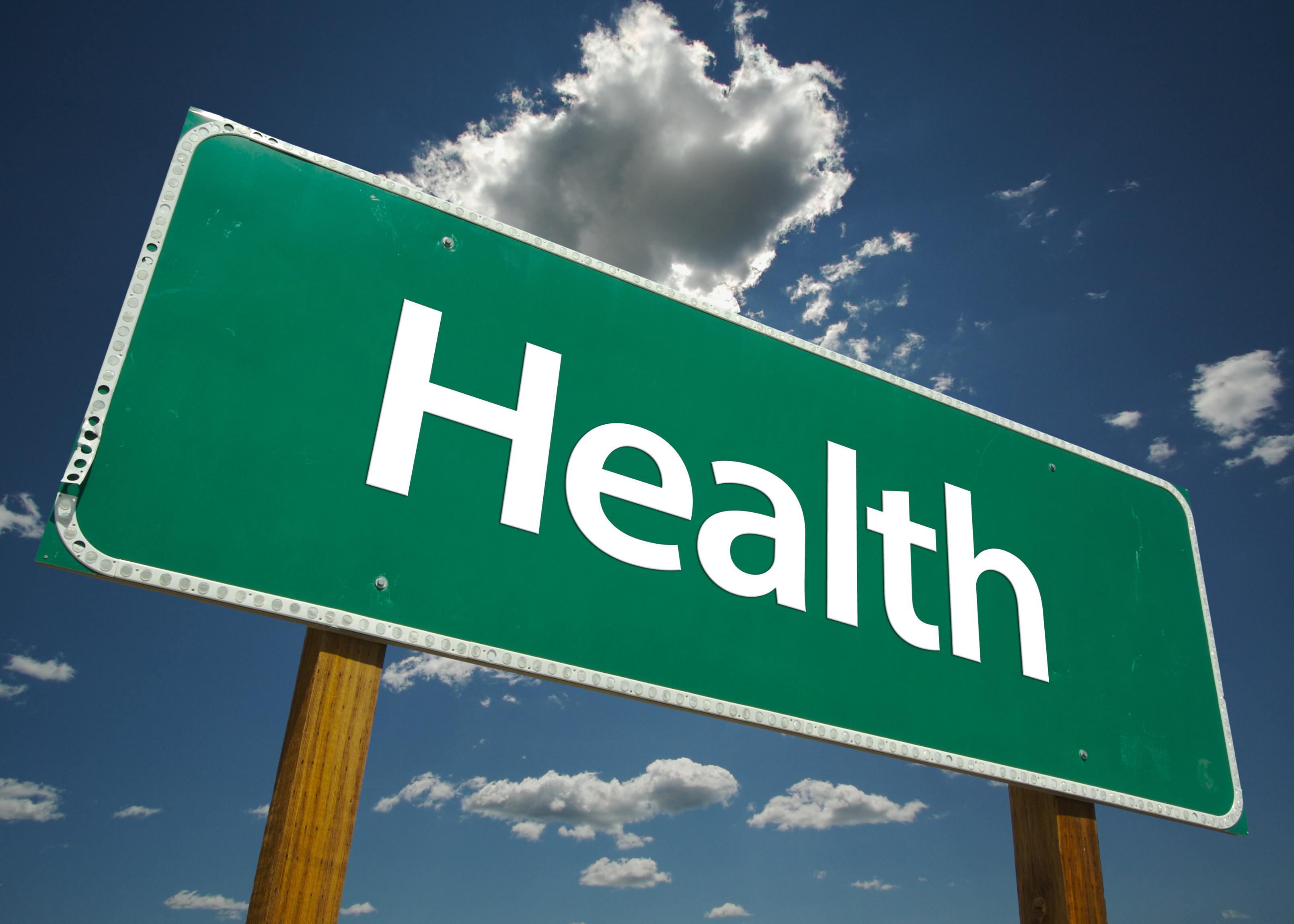 A green road sign with the word “Health” is pictured against a blue sky with white clouds.