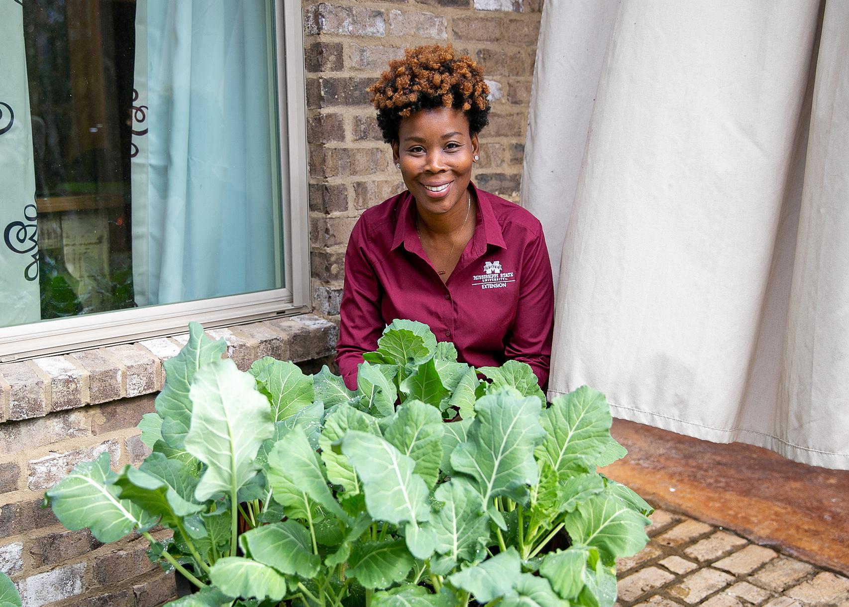 A woman sits on a patio behind a container where greens are growing.