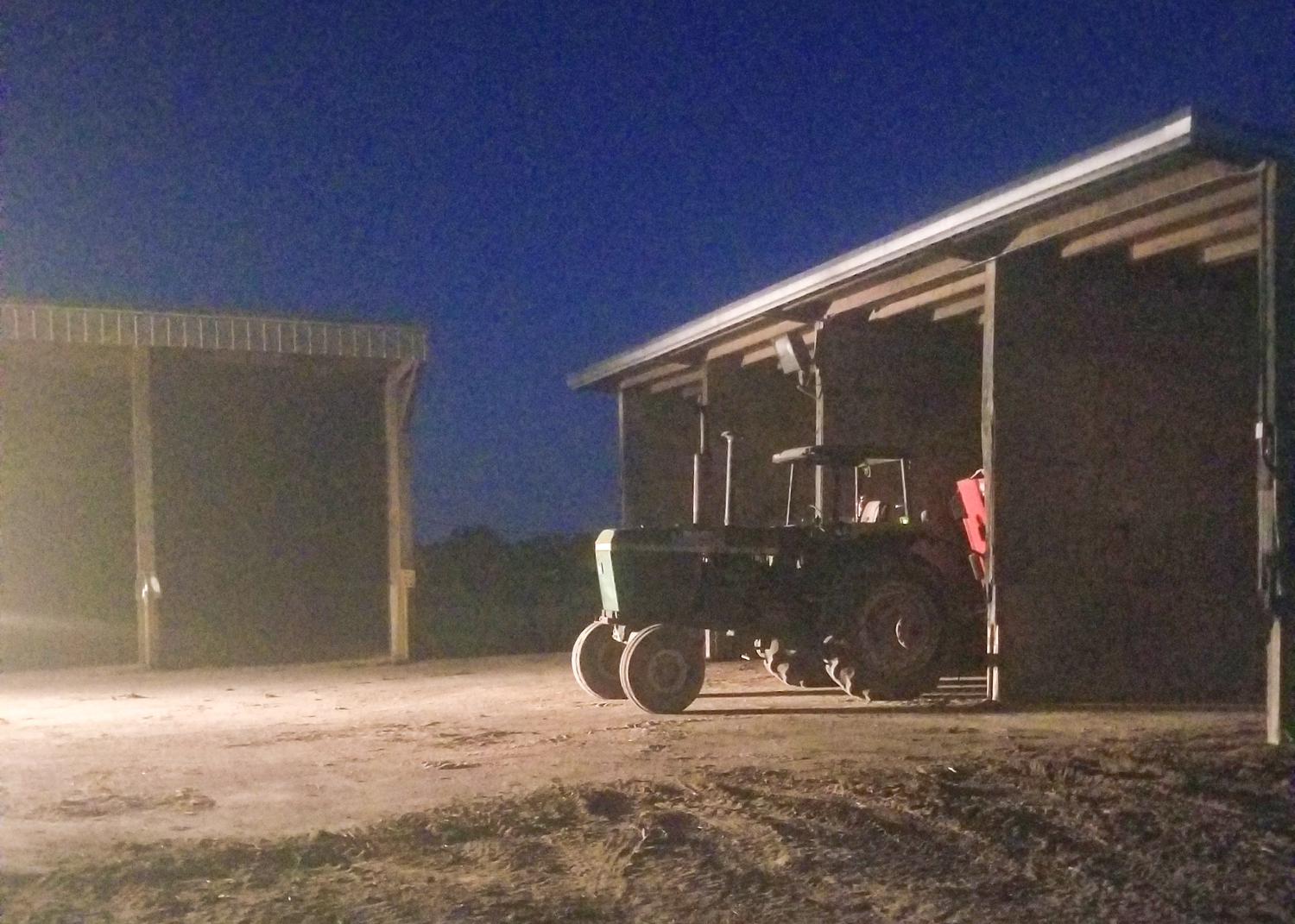 A tractor parked outside of a shed at night.