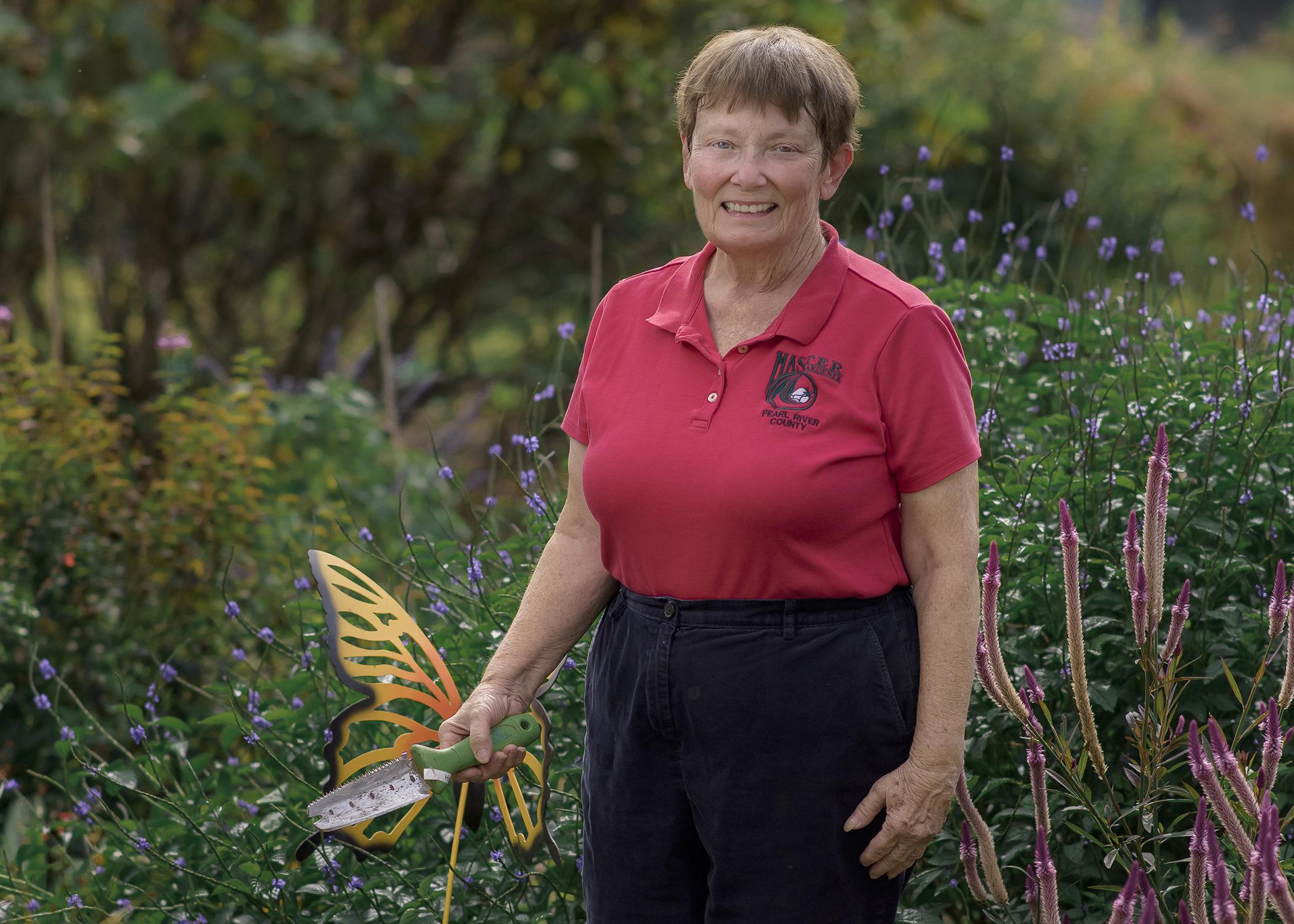 A woman holding a gardening tool stands in a green landscape.