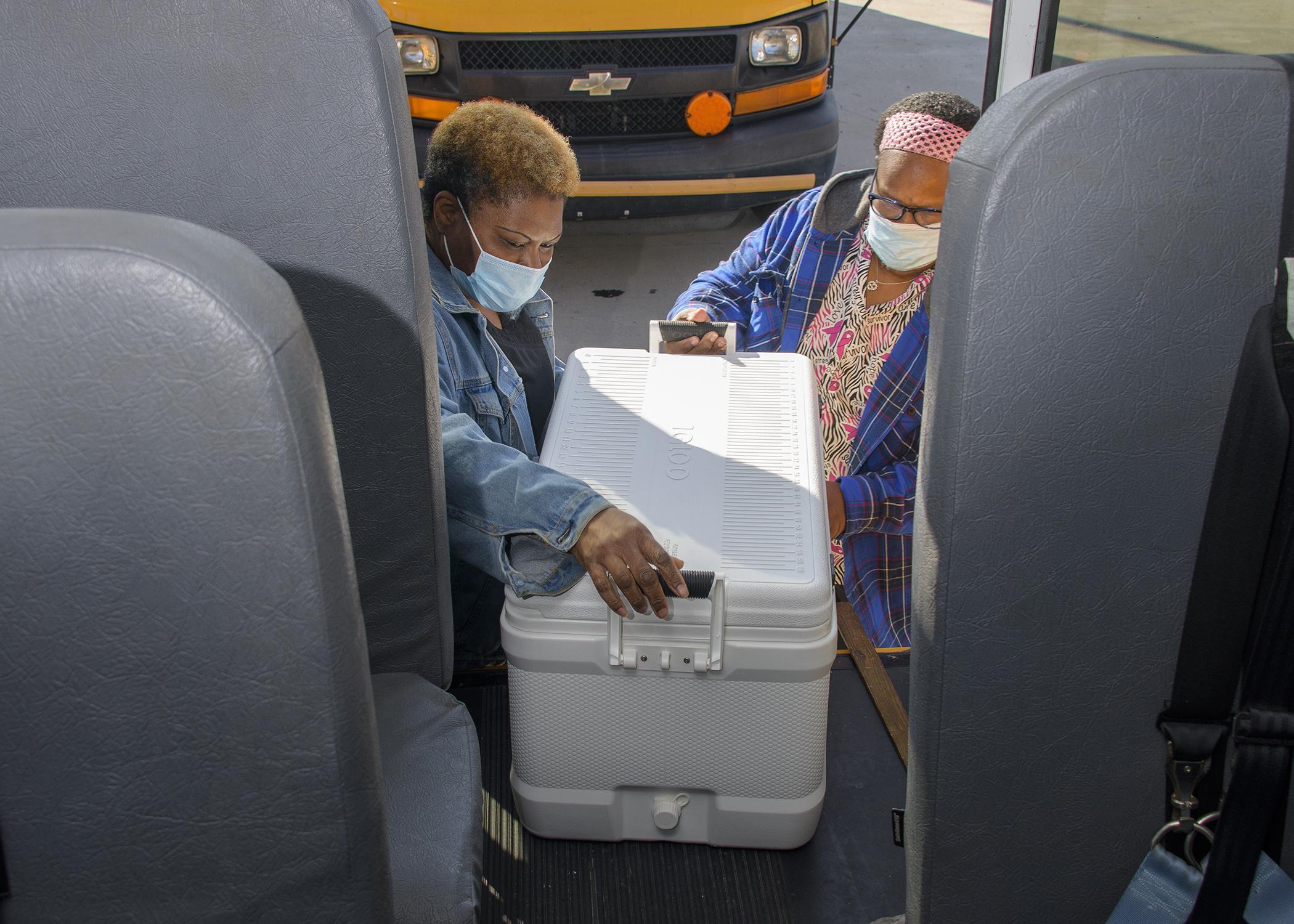 Two women load an ice chest on a bus.