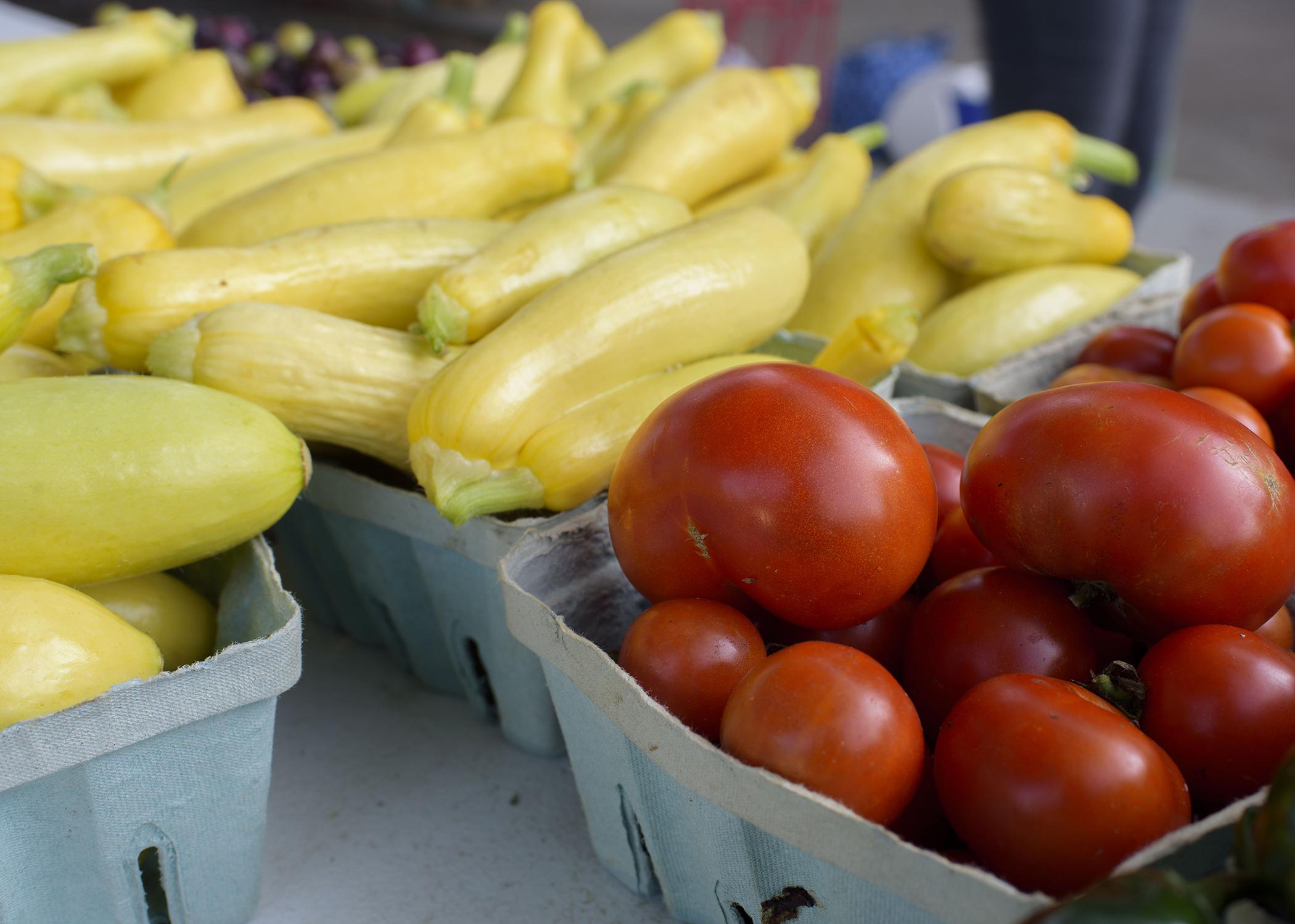 Close up of tomatoes and yellow squash in farmers market baskets.