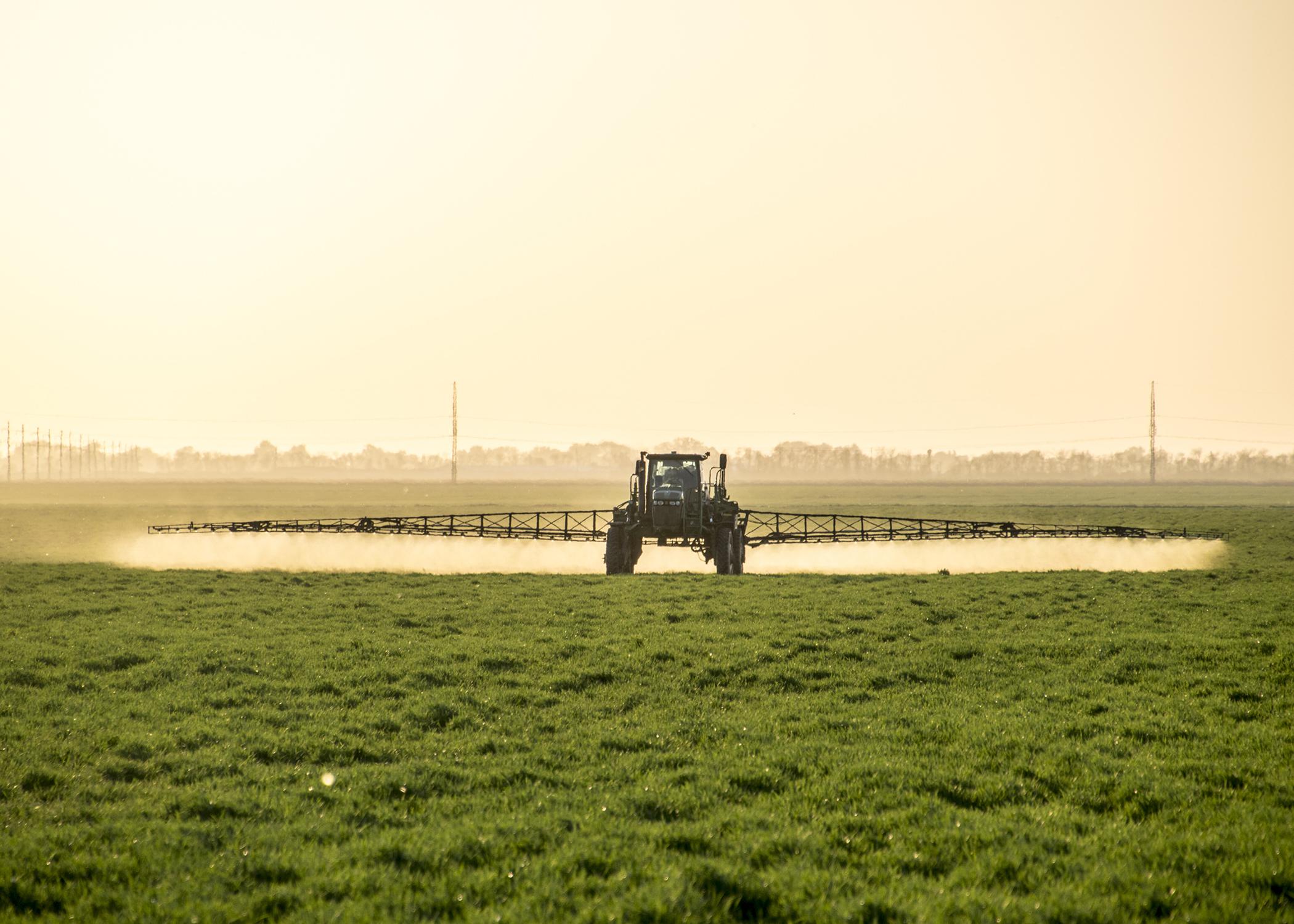 A tractor with a boom arm sprays crops.