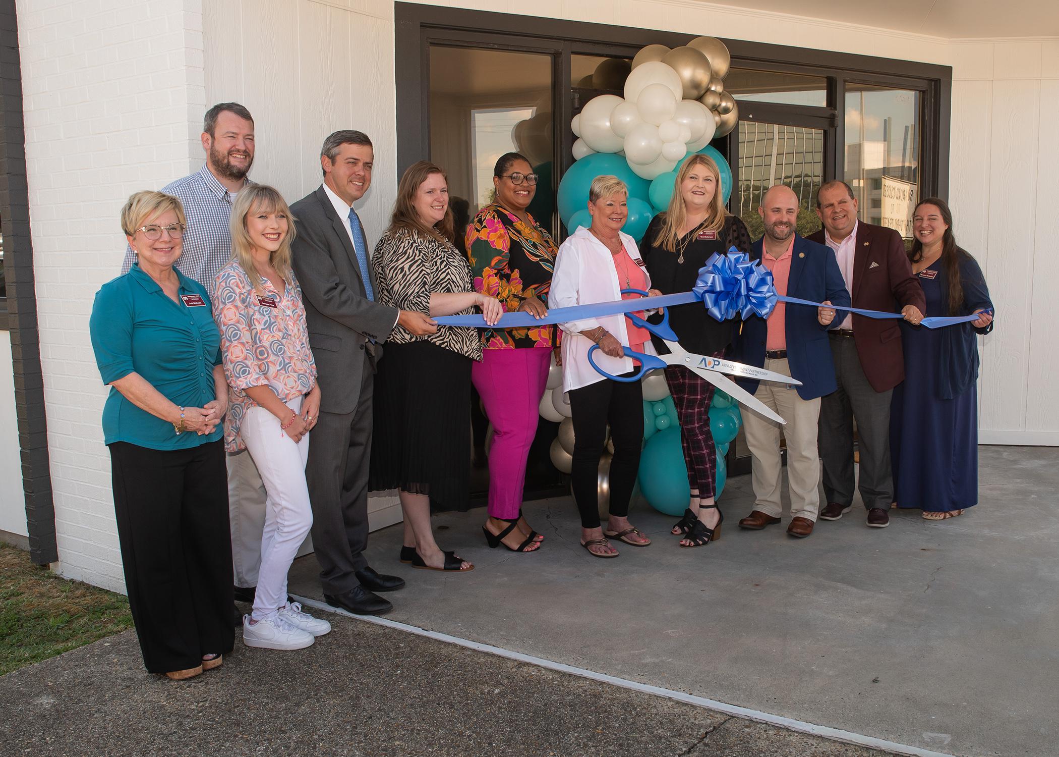 A group of people hold a ribbon in front of a building entrance.