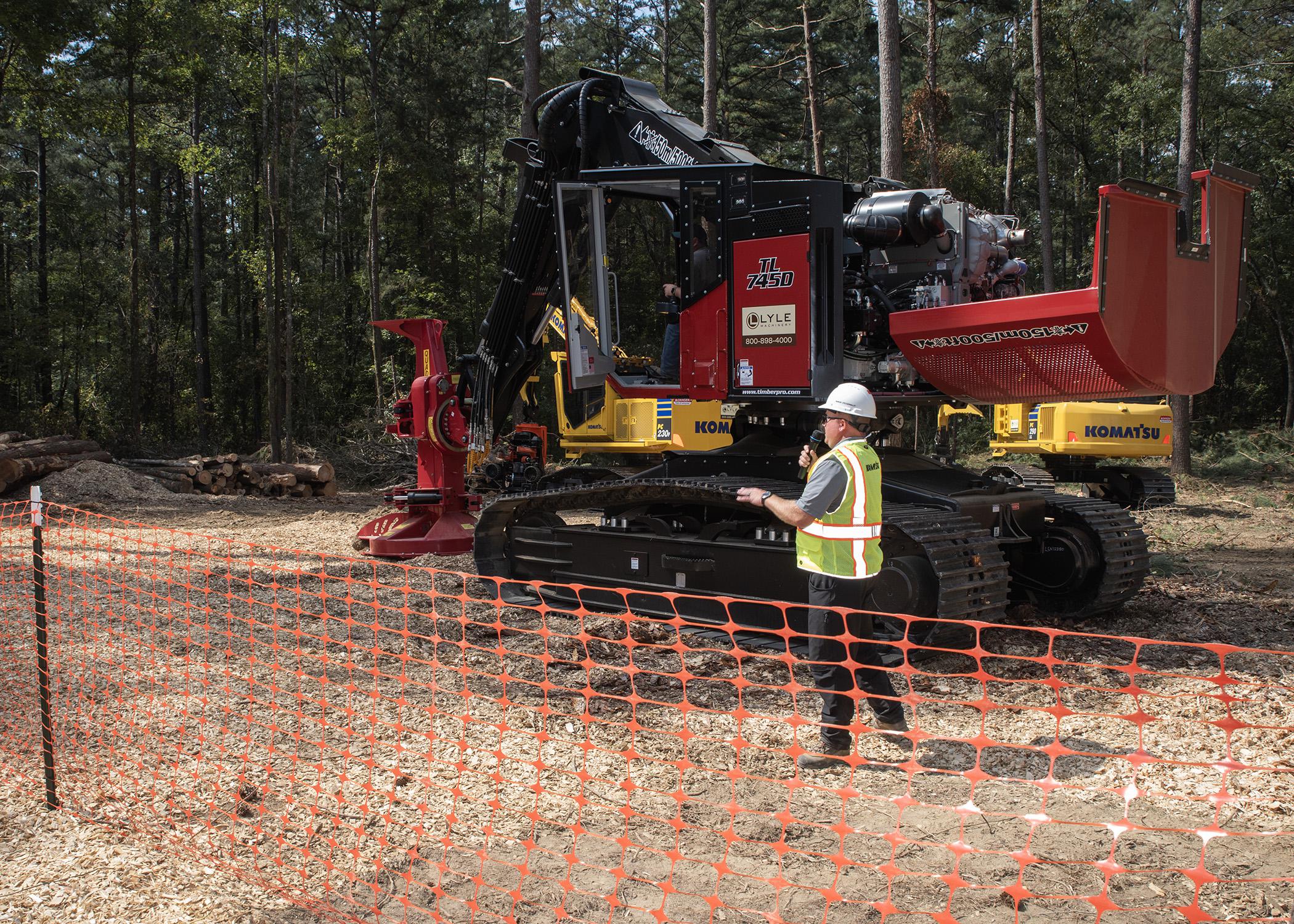 A man wearing a hard hat talking into a microphone in front of a piece of heavy equipment.