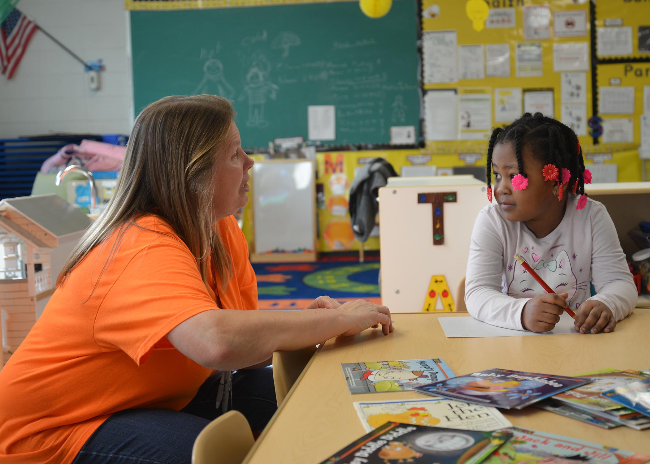 A teacher speaks to a child in a classroom.