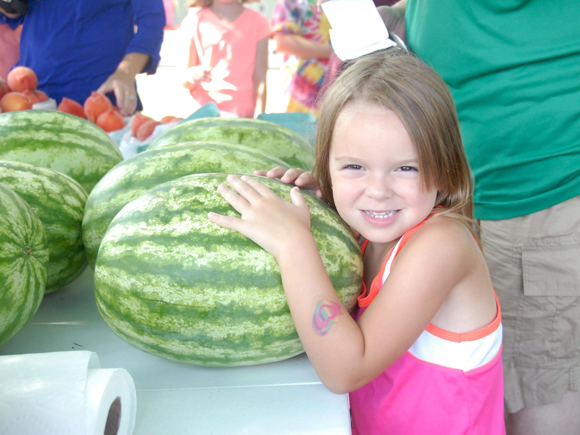 Emily Grace Barnette is ready to take this watermelon home from the Starkville Community Market on June 21, 2016. (Photo by MSU Extension Service/Linda Breazeale)