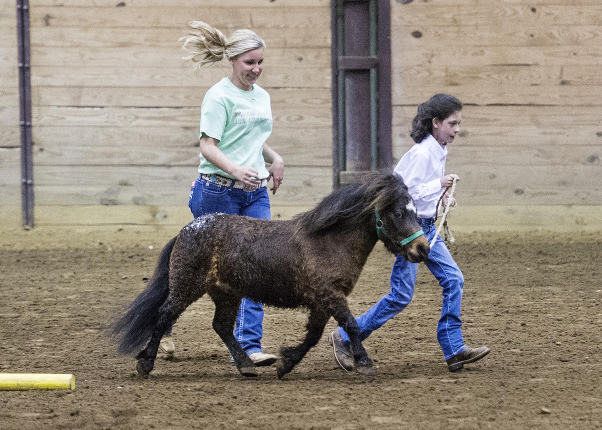 Cassie Brunson, coordinator of the Mississippi State University Extension Service Therapeutic Riding and Activity Center, runs beside Little Sam, led by Paige Davis Linley, 10, a participant in the first Therapeutic Riding Expo, held Tuesday night (April 14) at the Mississippi Horse Park near Starkville, Miss. (Photo by MSU Public Affairs/Megan Bean)