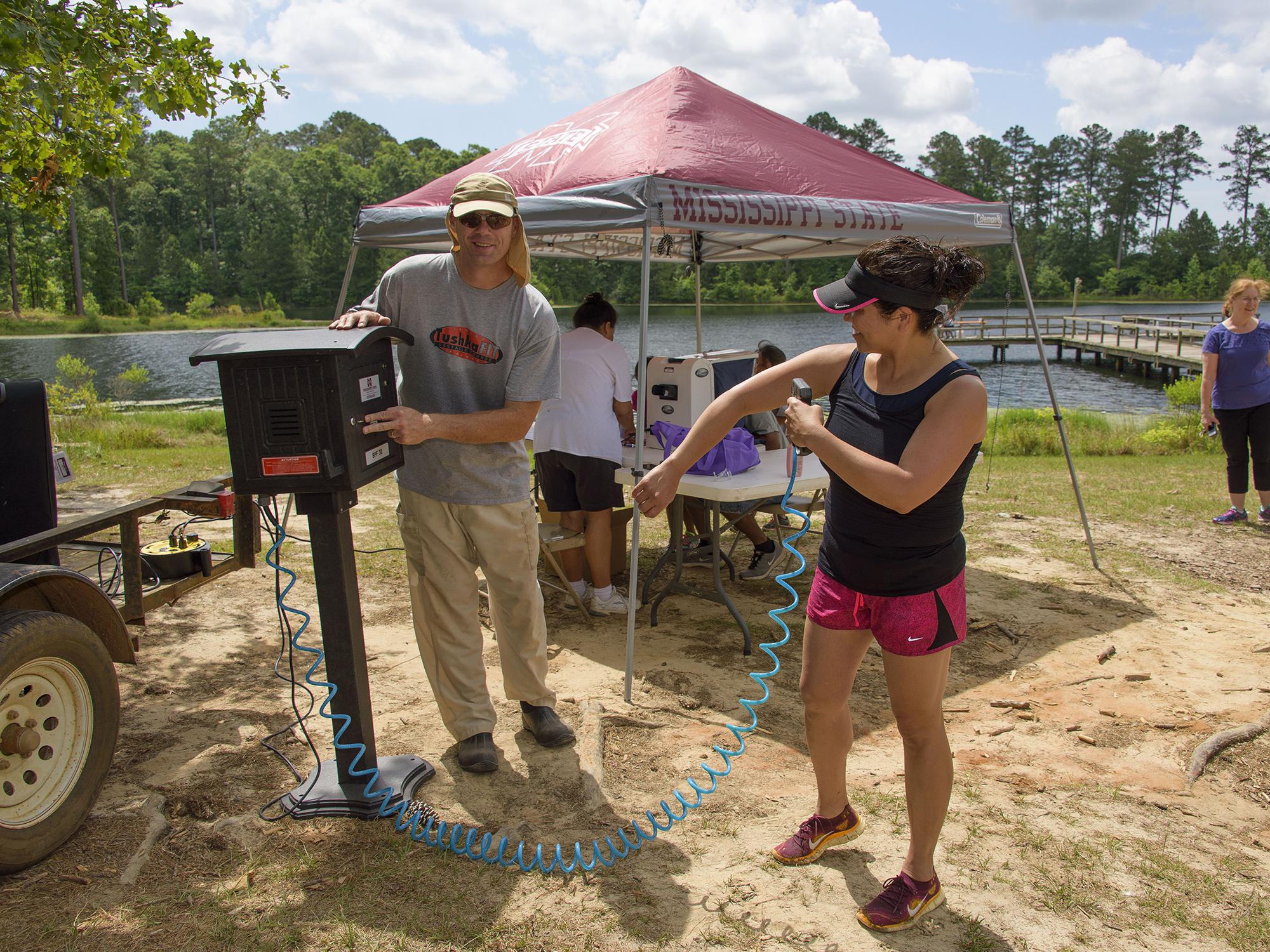 Jim McAdory, Mississippi State University Extension Service agent to the Mississippi Band of Choctaw Indians, shows Natasha Willis how to use the sunscreen dispenser provided by MSU Extension. The demonstration was part of a May 28 boating event in Neshoba County, Mississippi. (Photo by MSU Extension Service/Kevin Hudson)