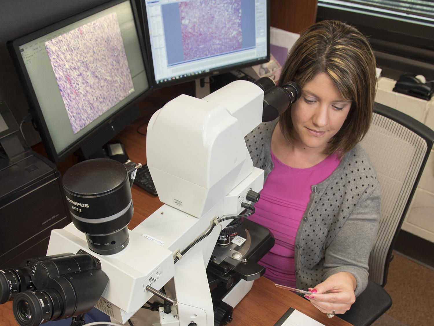 Dr. Alicia Olivier, an assistant professor in the Mississippi State University College of Veterinary Medicine, prepares to view a histology slide from a necropsy under a microscope. MSU offers this service to help determine causes of death for animals. (Photo by MSU-CVM/Tom Thompson)