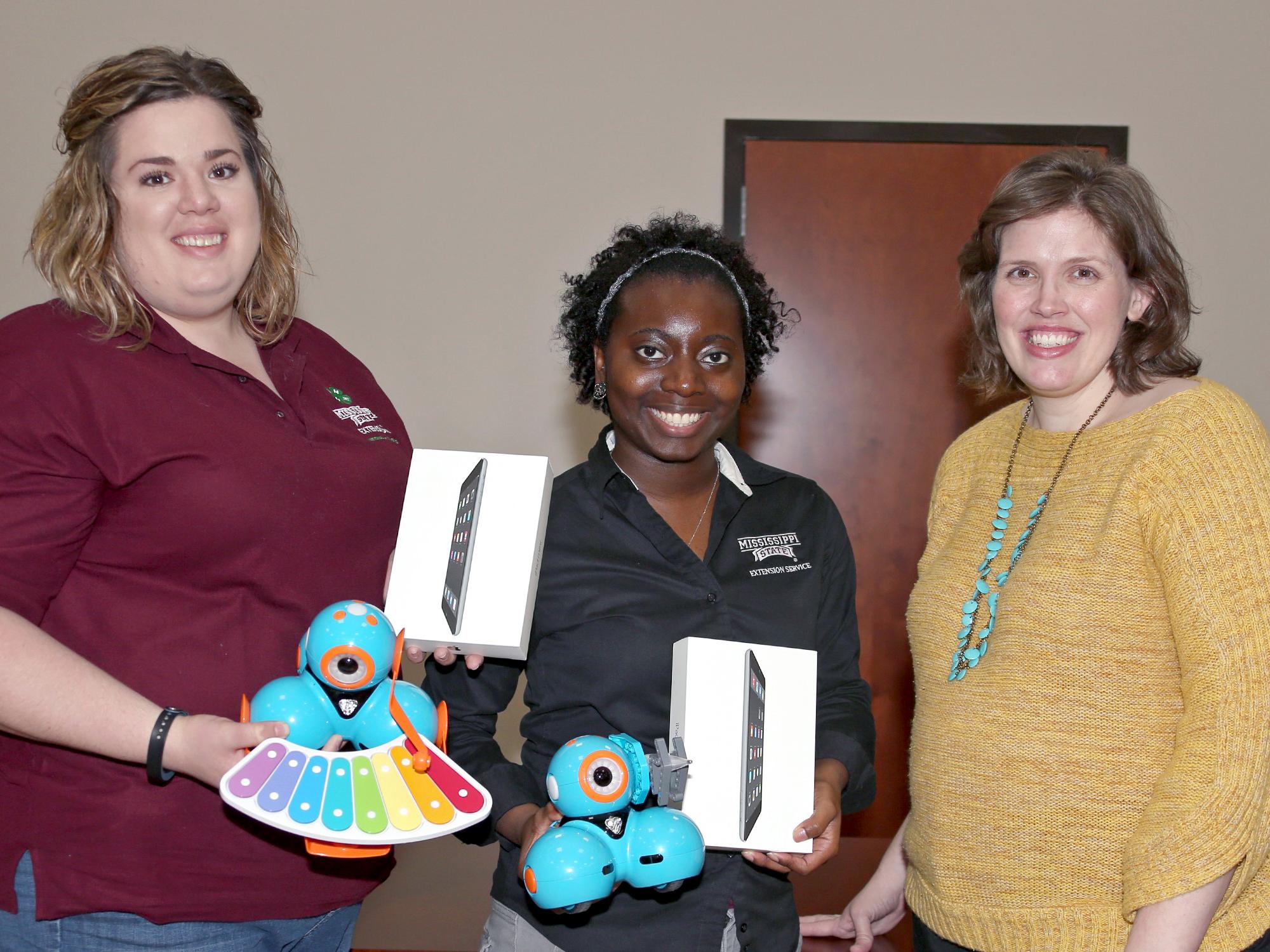 Mississippi State University Extension Service agents Jennifer Williams of Webster County, left, and Monet Kees of Pearl River County hold Dash & Dot interactive robots used by young 4-H’ers to learn STEM concepts. At right is Mariah Smith, an assistant Extension professor with the Center for Technology Outreach. Smith developed a curriculum last year that uses the robots along with mini iPads, all of which were funded through a $14,000 grant from the Verizon Foundation. (Photo by MSU Extension Service/Kat 