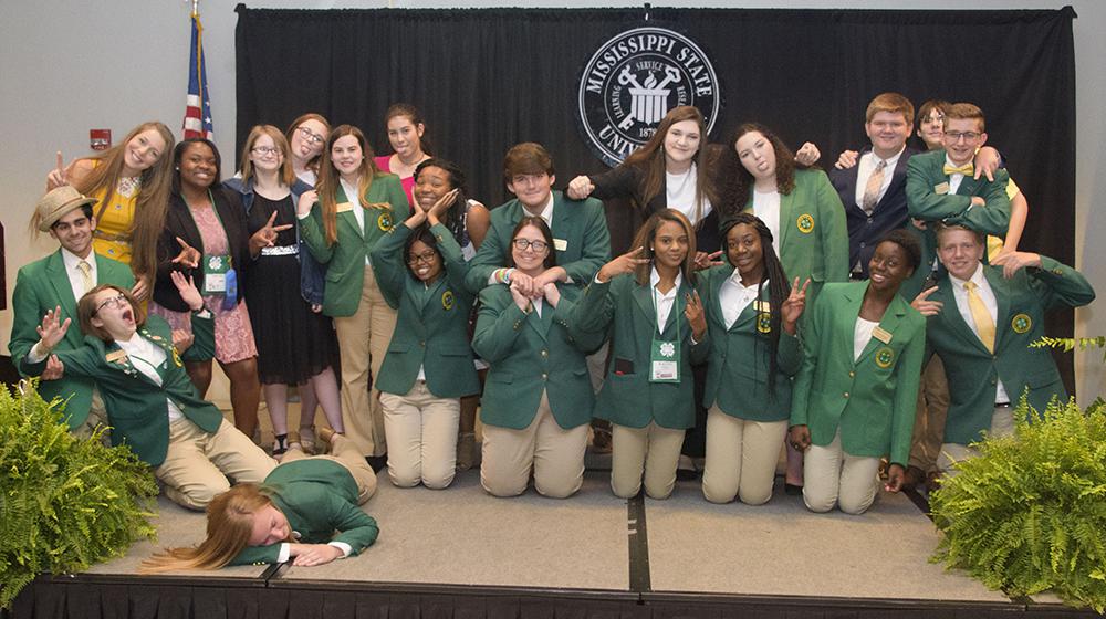 Twenty-one teens, most of whom are wearing green sport jackets, make silly faces for the camera.