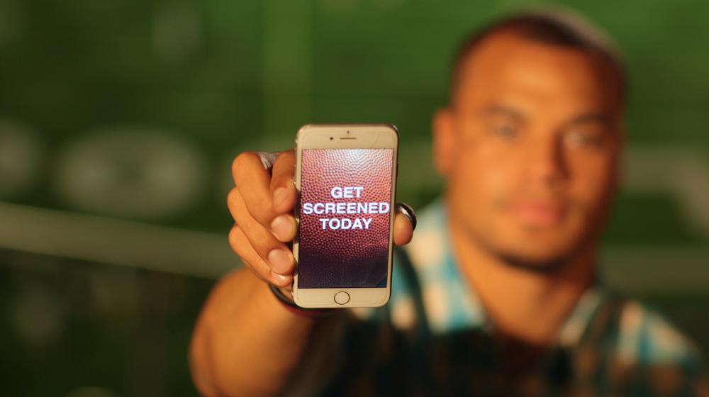 Dak holding phone with message "Get screened today" during the Colon Cancer Screening PSA shoot.