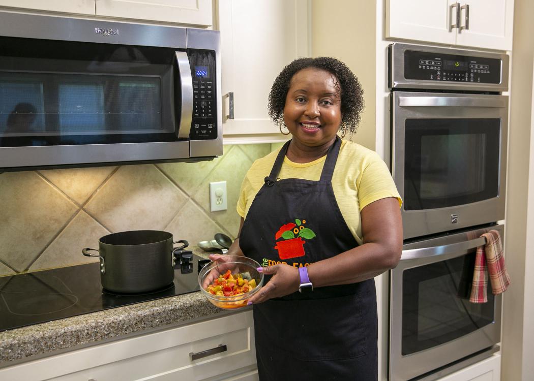 A woman stands in front of the stove with a bowl of Catfish Gumbo.