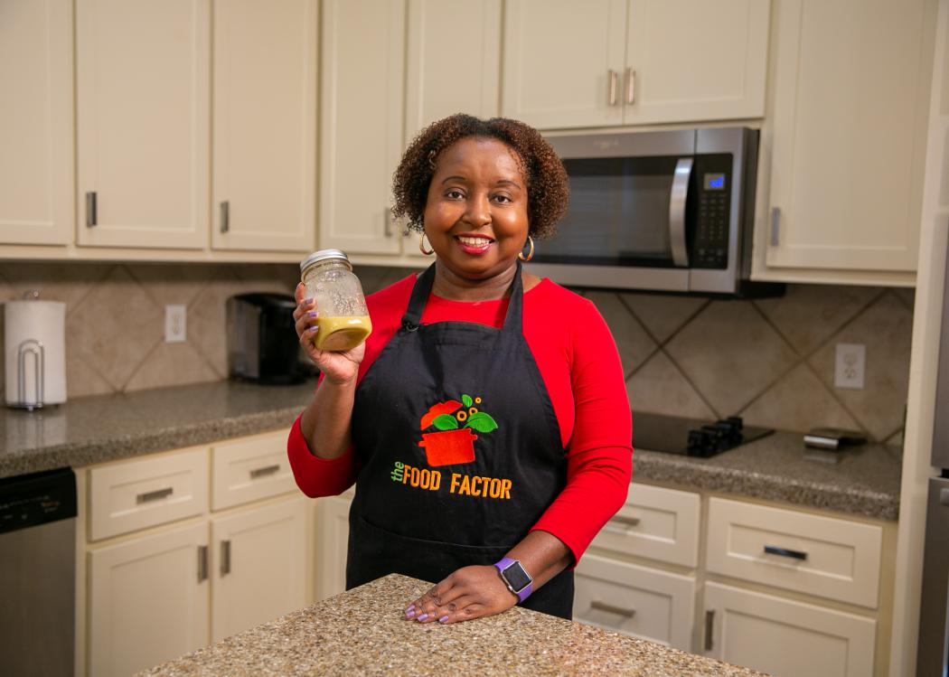 A woman holds a jar of Honey Mustard Dressing in a kitchen.