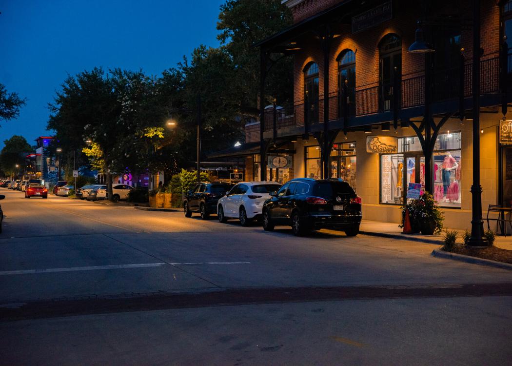 A night view of a downtown street in Ocean Springs, Mississippi, lined with shops and parked cars.