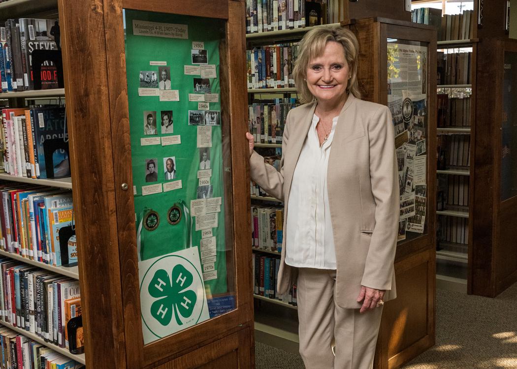 U.S. Senator Cindy Hyde-Smith stands next to a display case in a library.