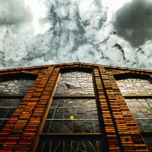 Worm's eye view of building with stained glass windows with cloudy sky.