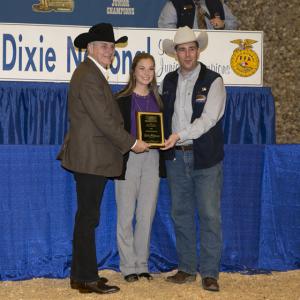  A teenage girl stands in between two men wearing cowboy hats and holding a plaque in front of her.
