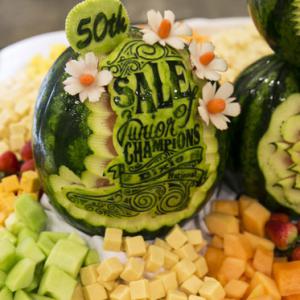 A green watermelon with the words “50th Sale of Junior Champions Dixie National” and other designs rests in the middle of assorted bite-sized foods.