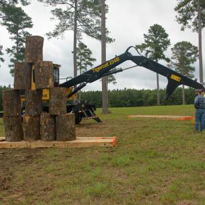 Two men standing beside a loader and stack of logs.