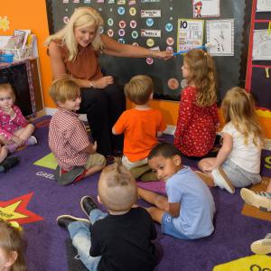 A woman pointing to a display with toddlers watching.