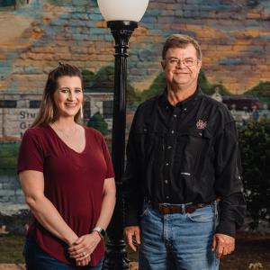 A woman and a man standing in front of a mural and lamppost.