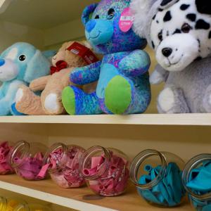 Two shelves, with stuffed animals on the top and colorful balloons in clear, plastic holders on bottom.