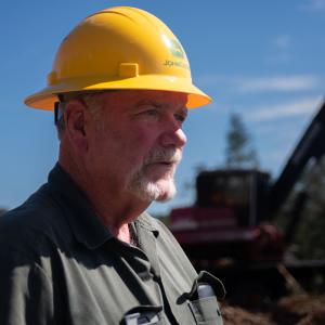 A man wearing a hardhat standing in front of a tractor.