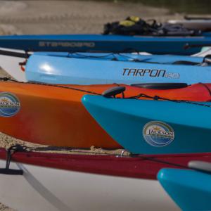 Blue, orange, and white kayaks sitting on sand.
