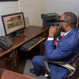 A man wearing a suit and seated at a desk contemplates a computer.