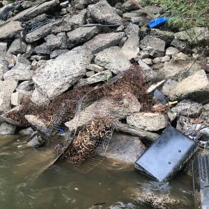 Trash piled up on a rocky bank at the edge of shallow water.