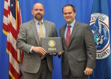 Two men on a stage holding a FEMA certificate and looking at the camera.