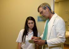 A teenage girl looks on as a doctor explains a chart in his hands.