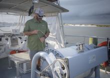 A man stands on a boat and checks a large roll of fishing line.