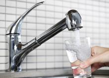 Water flows from a stainless steel kitchen faucet into a clear drinking glass.