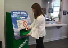Young woman places a prescription bottle in secure slot in a large, green metal box