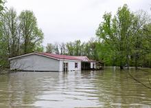 Flood waters surround the bottom third of a mobile home with trees in the background.