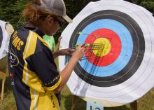 A 4-H’er wearing sunglasses tallies arrows in a colorful paper archery target.